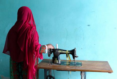 Rahima, a garment factory worker in Bangladesh, next to a sewing machine and with her back to camera
