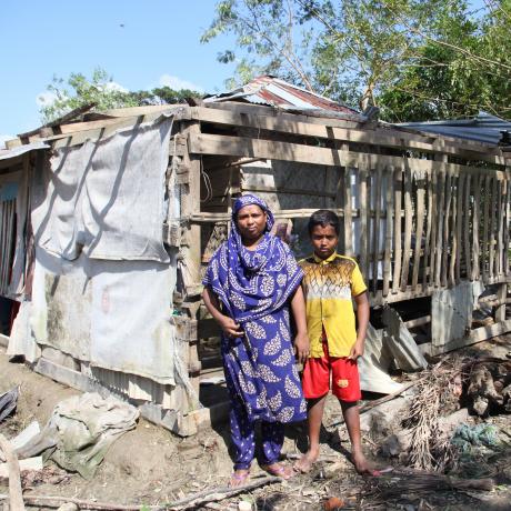 A mother and child stand outside their ruined home in Bangladesh