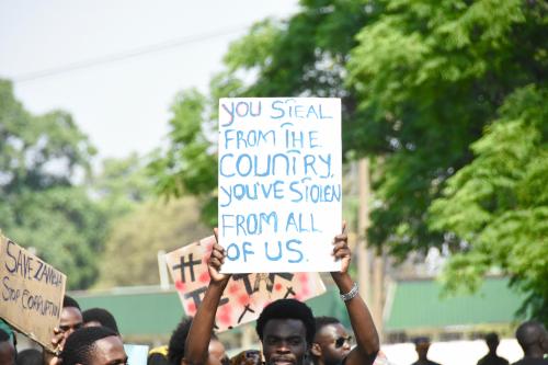 A protester holding a sign which reads: "You steal from the country. You've stolen from all of us."