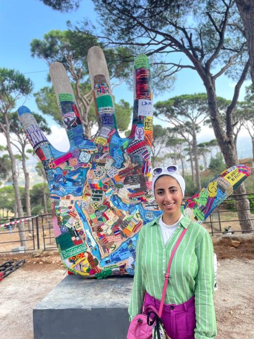 Photo shows a young woman in a green top standing next to an embroidered hand