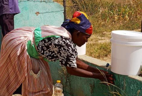 A woman in rural Zimbabwe washes her hands from a plastic container 