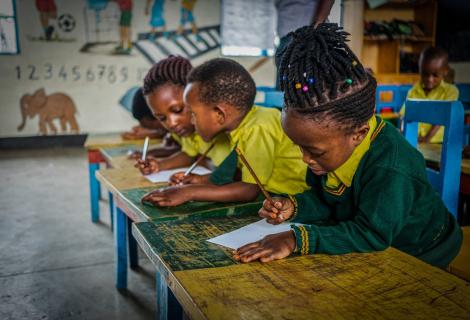 A little girl, Freza 5, in a classroom in Rwanda sitting at a desk, other children in the background