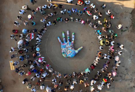 Photo is an aerial view of an embroidered hand surrounded by a crowd of young activists