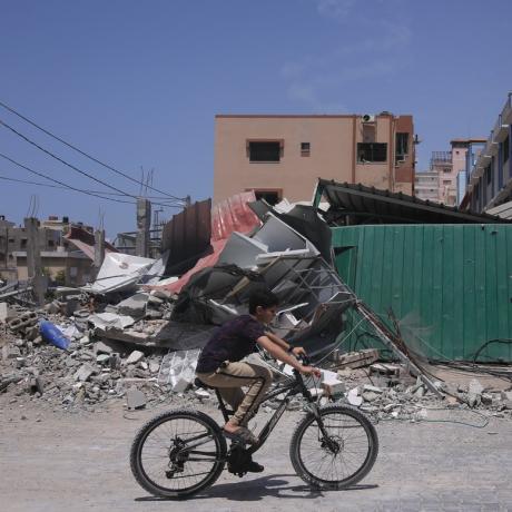 A boy rides his bike past buildings destroyed by airstrikes in Gaza