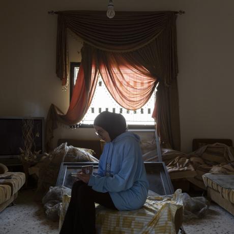 A young woman from Lebanon looks at a family photo album in her living room, which was damaged after it was bombed by Israeli forces.