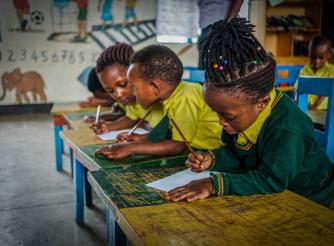 A little girl, Freza 5, in a classroom in Rwanda sitting at a desk, other children in the background