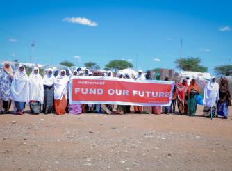 Women hold a banner saying fund our future. 