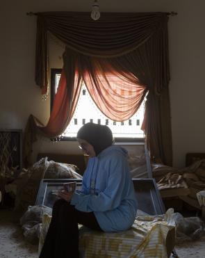 A young woman from Lebanon looks at a family photo album in her living room, which was damaged after it was bombed by Israeli forces. 